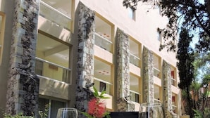 Mesa de café da manhã com ovos mexidos, torradas e frutas em um prato, acompanhadas por dois copos de suco de laranja, em frente a um edifício com colunas de pedra e uma varanda.