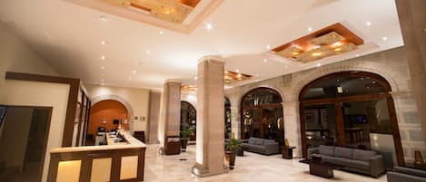 A spacious lobby with a reception desk, comfortable seating, and a high ceiling with recessed lighting.