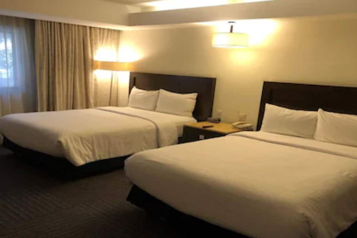 Ein Hotelzimmer mit zwei Betten, einem Nachttisch, einer Lampe und einem Fenster mit Vorhängen.