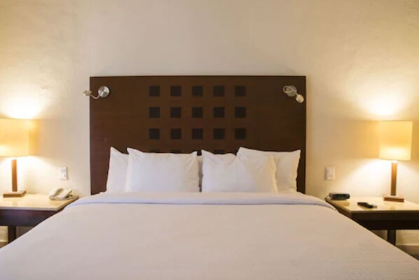 Una habitación de hotel con una cama grande, dos mesitas de noche con lámparas y un cabecero con diseño de cuadrícula.