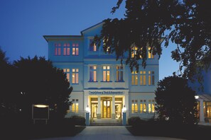 Un grand hôtel à plusieurs étages, doté d’une entrée imposante et de fenêtres illuminées.