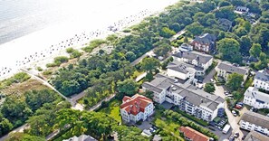Vue aérienne d’une zone résidentielle côtière, avec un grand ensemble d’immeubles, une plage où se trouvent des personnes et une végétation luxuriante.