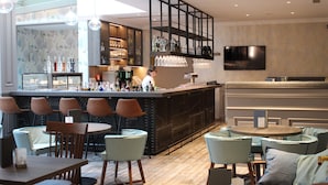 Uma área de bar com assentos, um barman e uma televisão presa na parede.