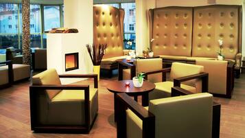A modern lounge area with leather sofas, a fireplace, and a view of the city through large windows.