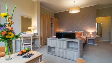 A modern hotel room with a wooden TV stand, a desk with a lamp, a chair, and a large mirror.