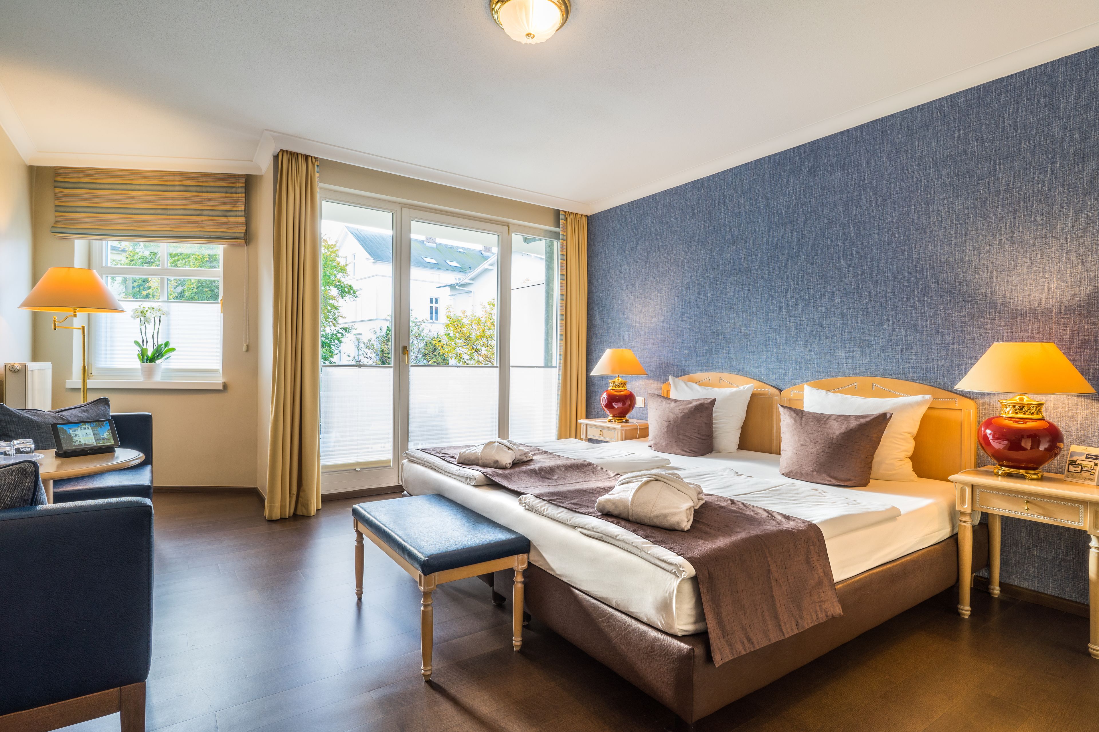 A hotel room with a large bed, bedside lamps, a desk with a laptop, and a view of the outdoors.