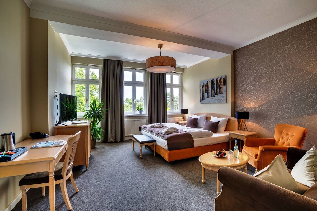 Ein Hotelzimmer mit Bett, Schreibtisch, Sessel, Sofa, kleinen Tisch und Fernseher.