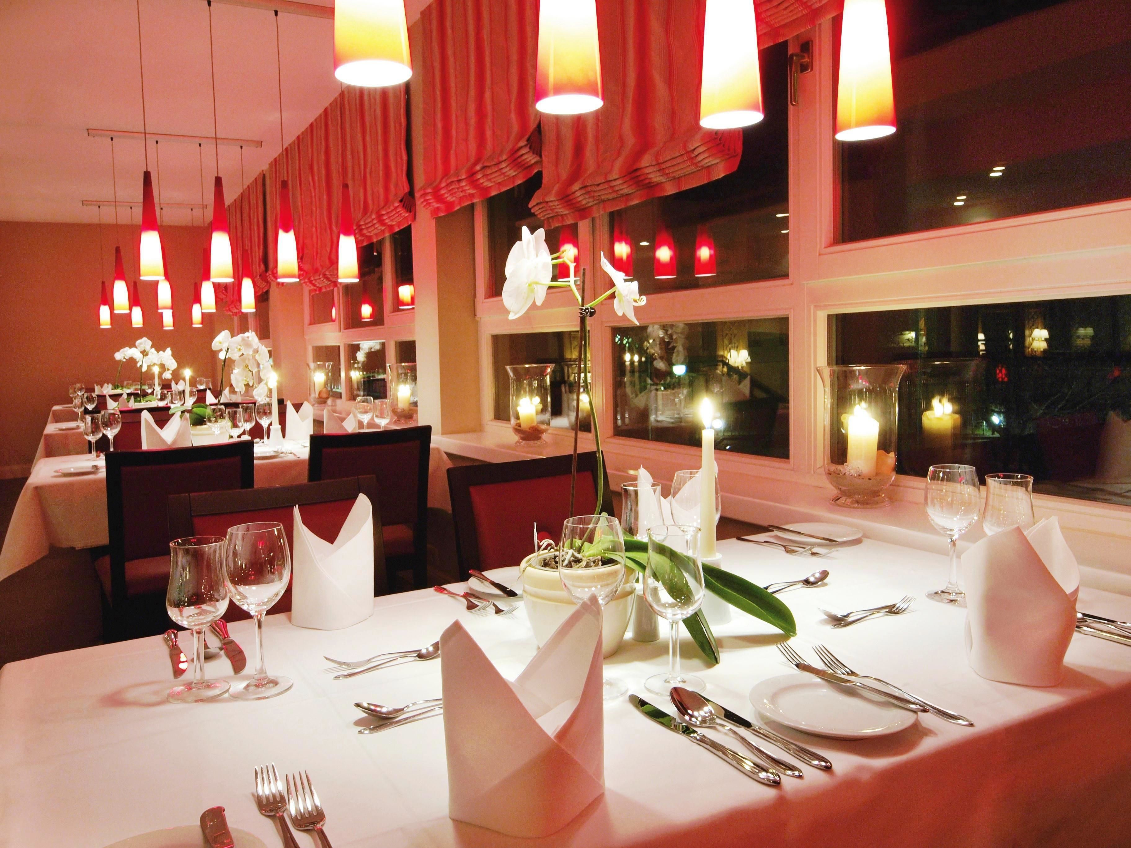 Un restaurant où les tables sont dressées pour le dîner, avec des bougies et des fleurs en décoration.