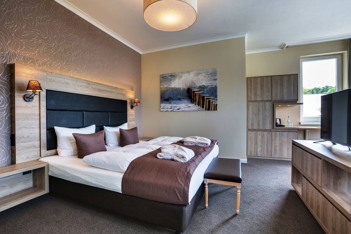 Ein modernes Hotelzimmer mit einem großen Bett, einem Holzkopfende, einem Gemälde von Wellen, einem Fernseher und einer Küchenzeile.
