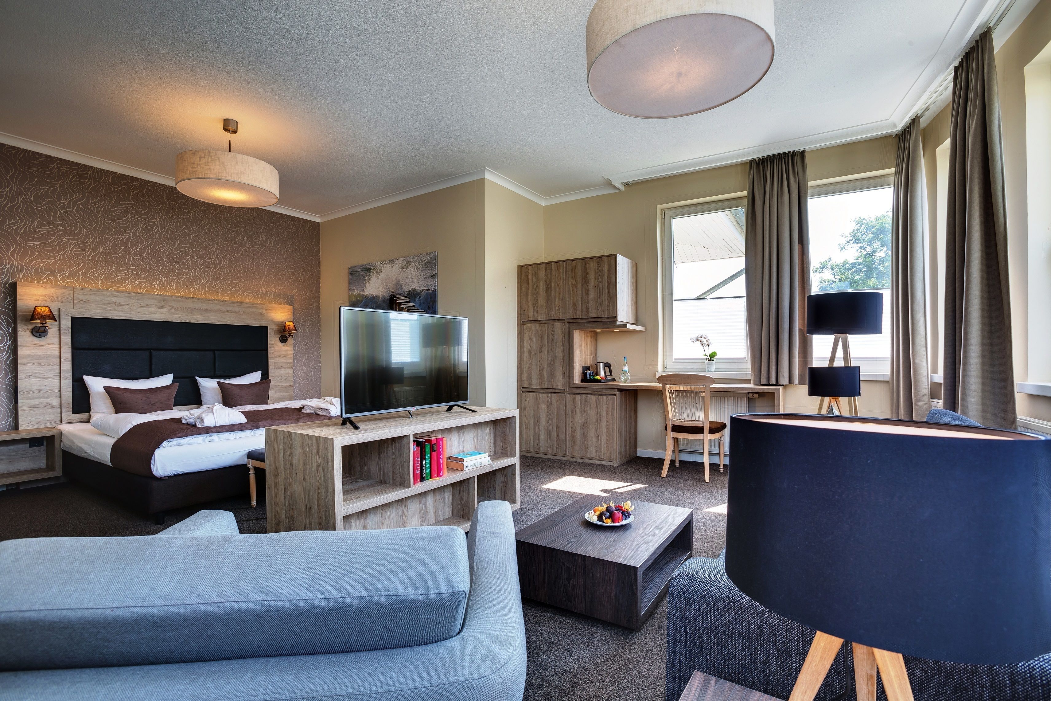 Ein modernes Hotelzimmer mit Bett, Fernseher, Sofa, Couchtisch und Schreibtisch.