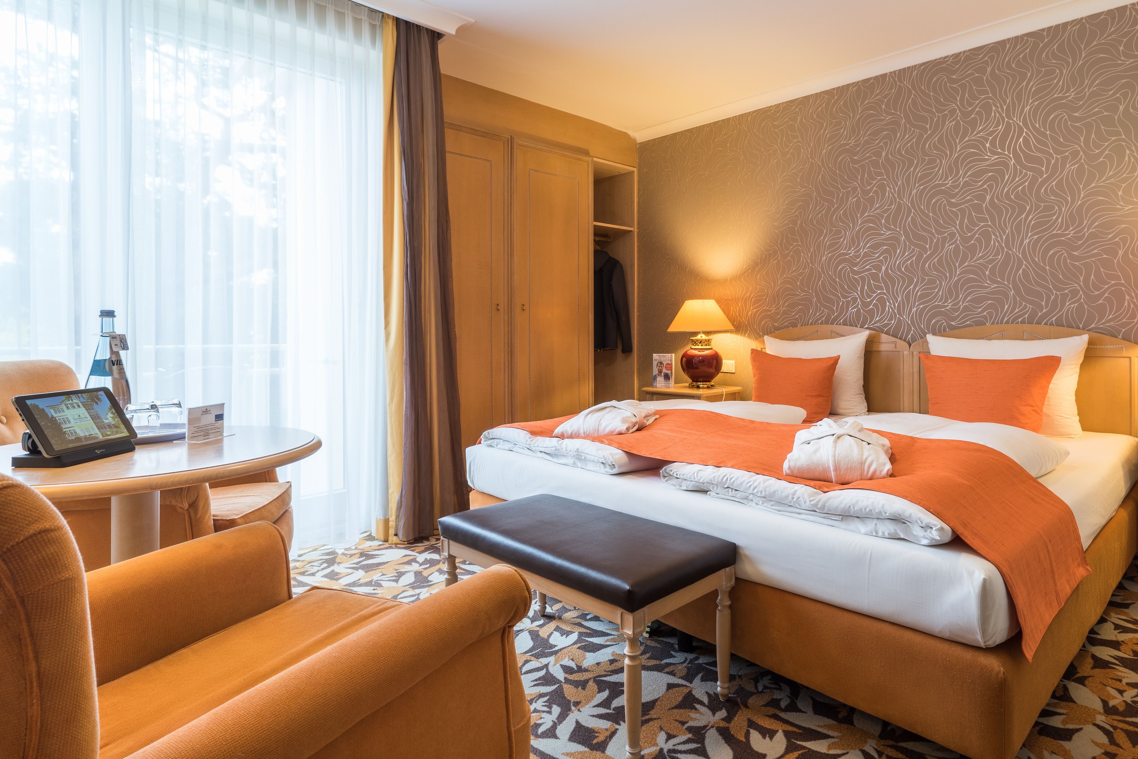 A hotel room with a bed, a desk, a chair, a bedside table, and a window with curtains.