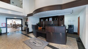 A hotel reception area with a reception desk, a clock, and a digital screen. - Prestige Prince George Lodge (Prince George)