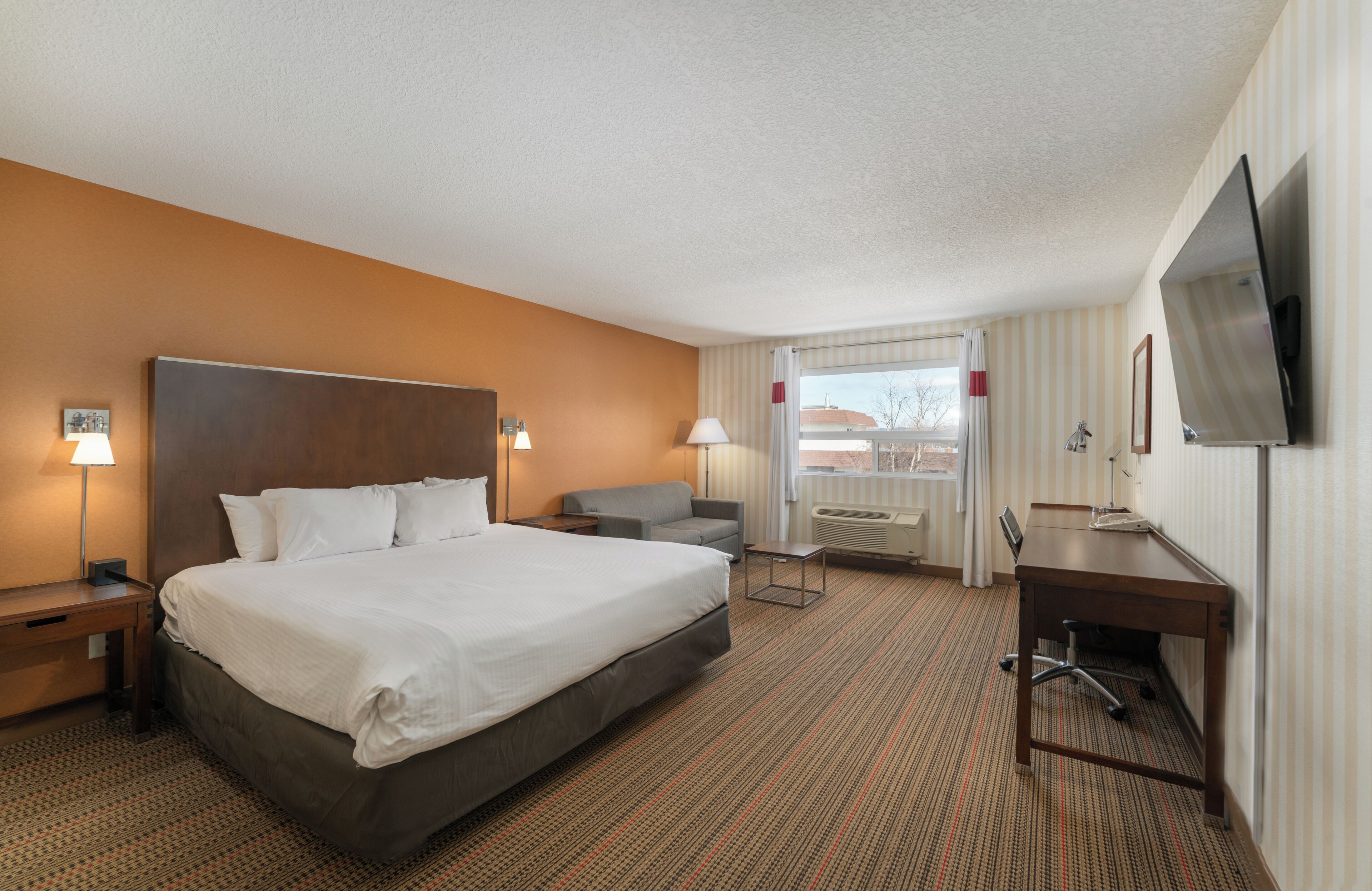 A hotel room with a large bed, a desk, a chair, a TV, and a window with curtains.