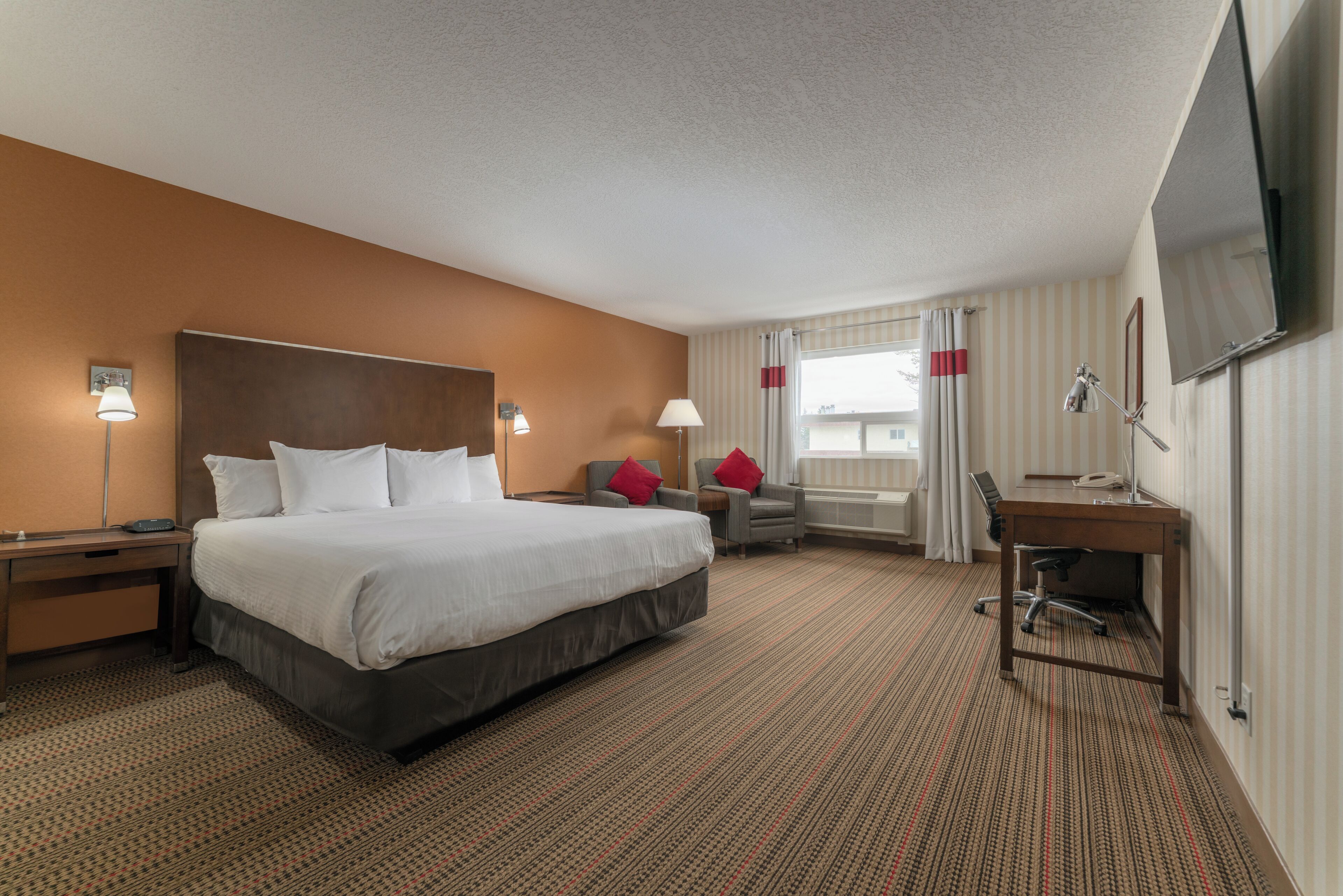 A hotel room with a large bed, a desk, a chair, a TV, and a window with curtains.