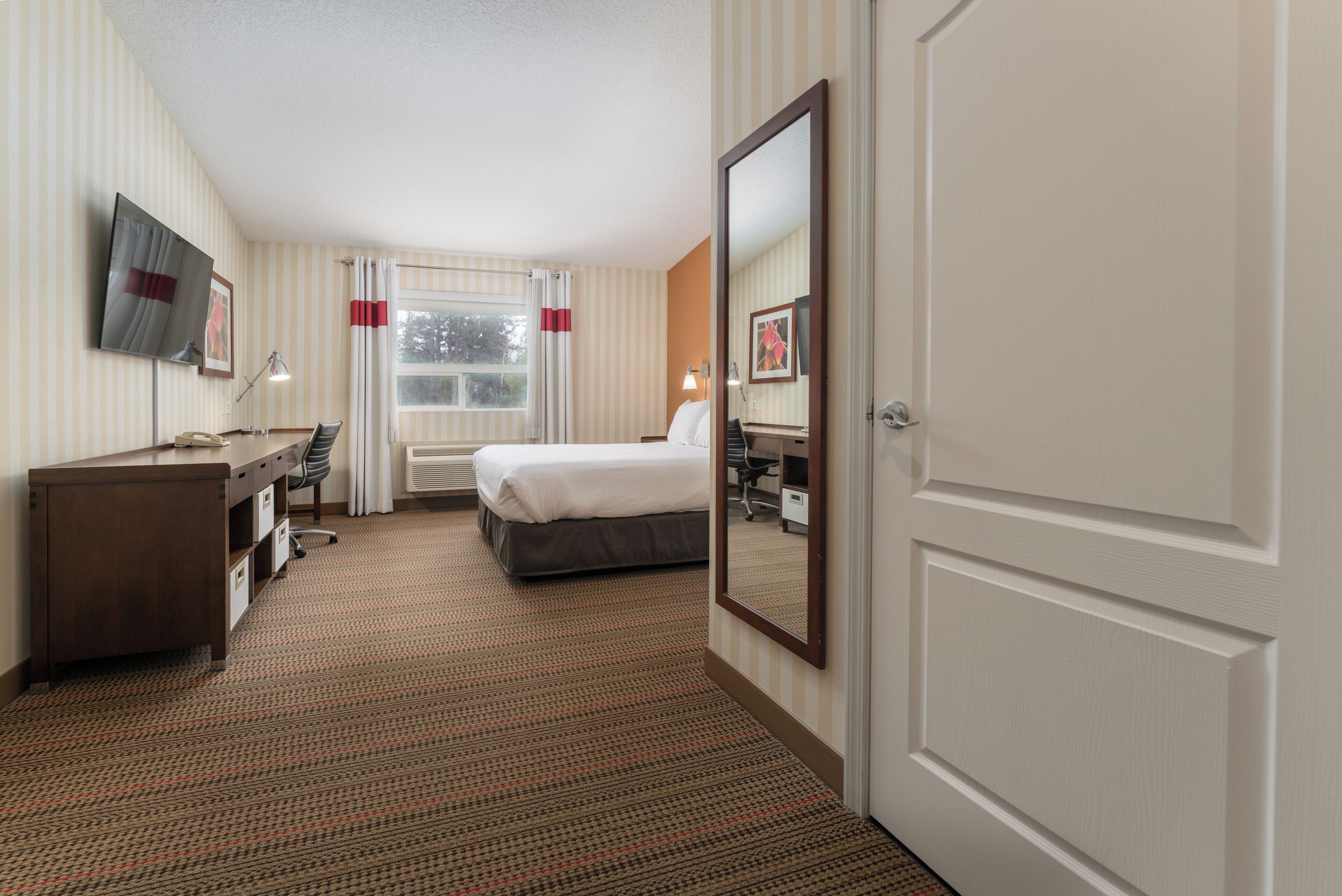 A hotel room with a bed, desk, chair, TV, and a large mirror.