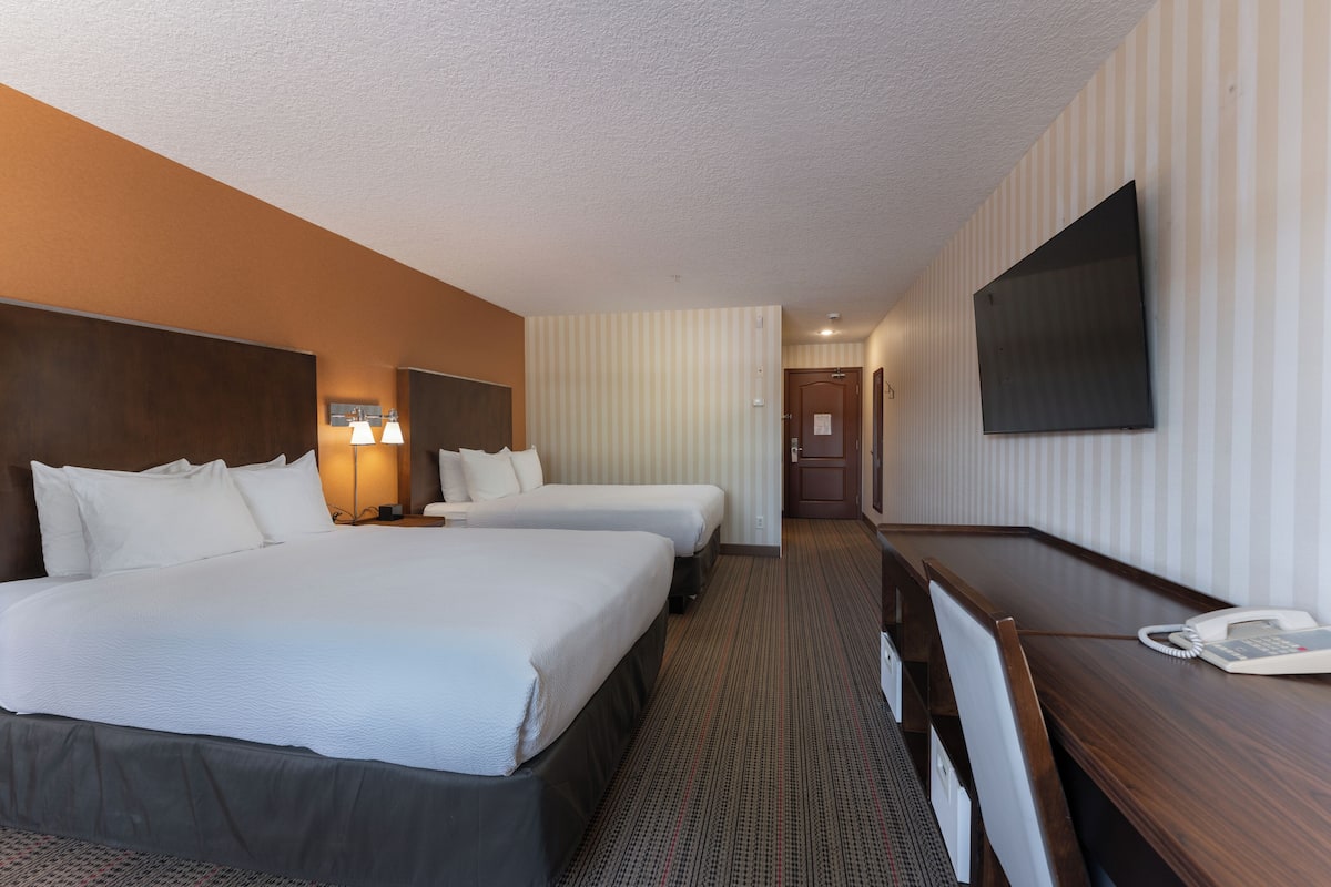 Ein Hotelzimmer mit zwei Betten, einem Schreibtisch mit Telefon und einem an der Wand befestigten Fernseher.