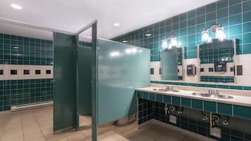 A restroom with teal tiles, two sinks, a mirror, and a glass partition.