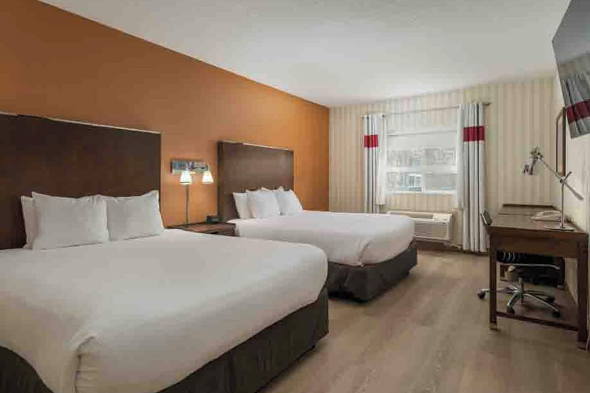 Ein Hotelzimmer mit zwei Betten, einem Schreibtisch, einem Stuhl, einem Fernseher und einem Fenster mit Vorhängen.