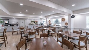 A spacious dining area with multiple tables and chairs, a kitchen in the background, and a sign on the wall. - Prestige Prince George Lodge (Prince George)