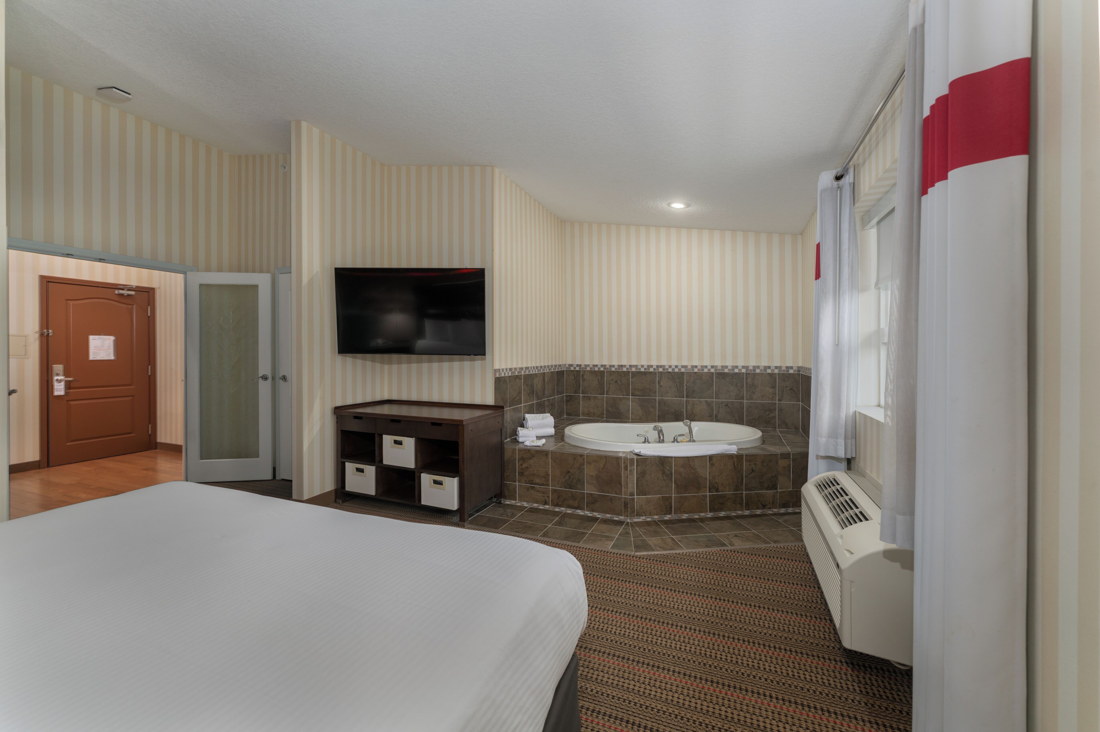 A hotel room with a bed, a bathroom with a bathtub, a television, and a door.
