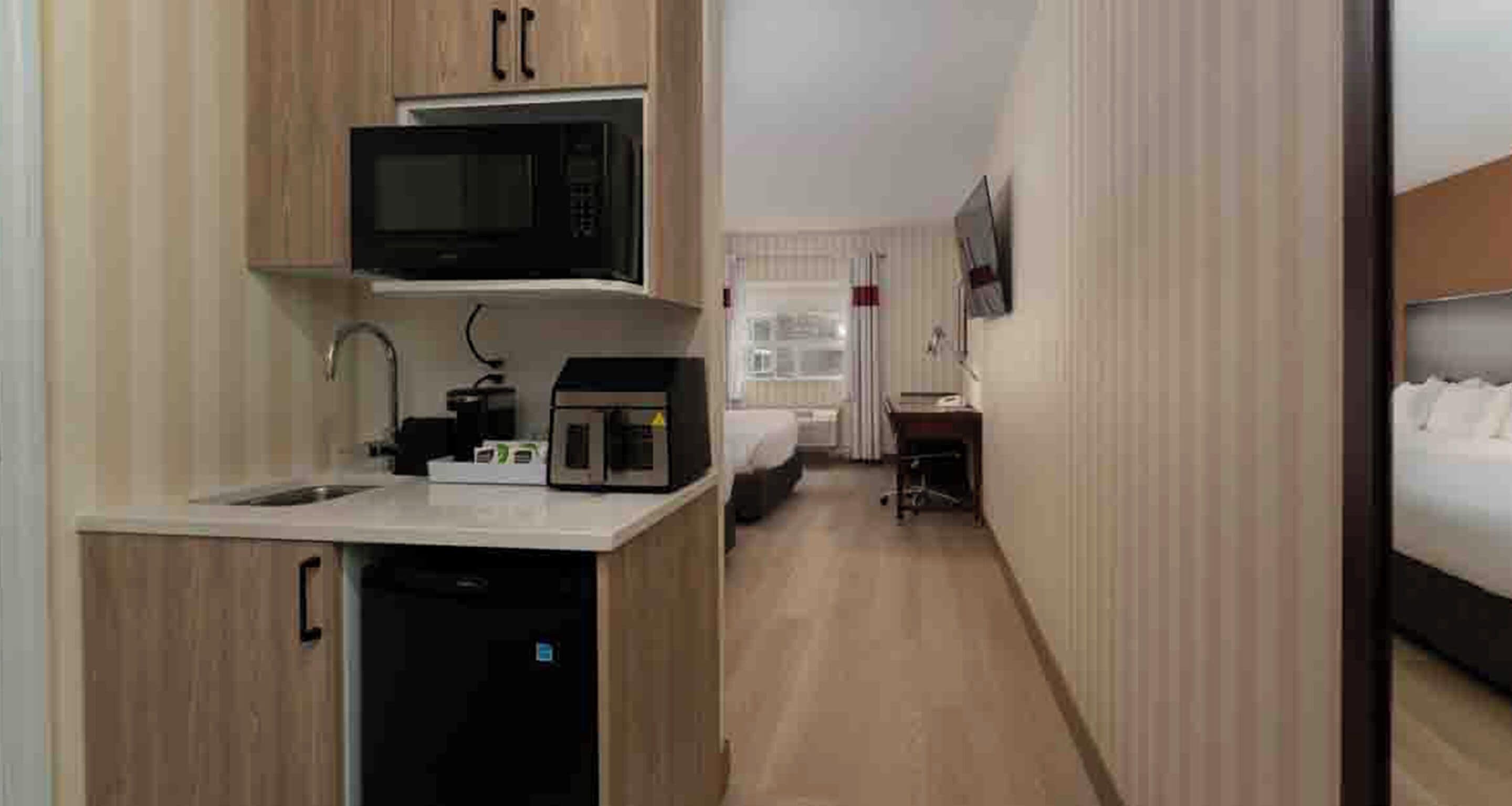 A compact hotel room with a kitchenette, a bed, a TV, and a bedside table.