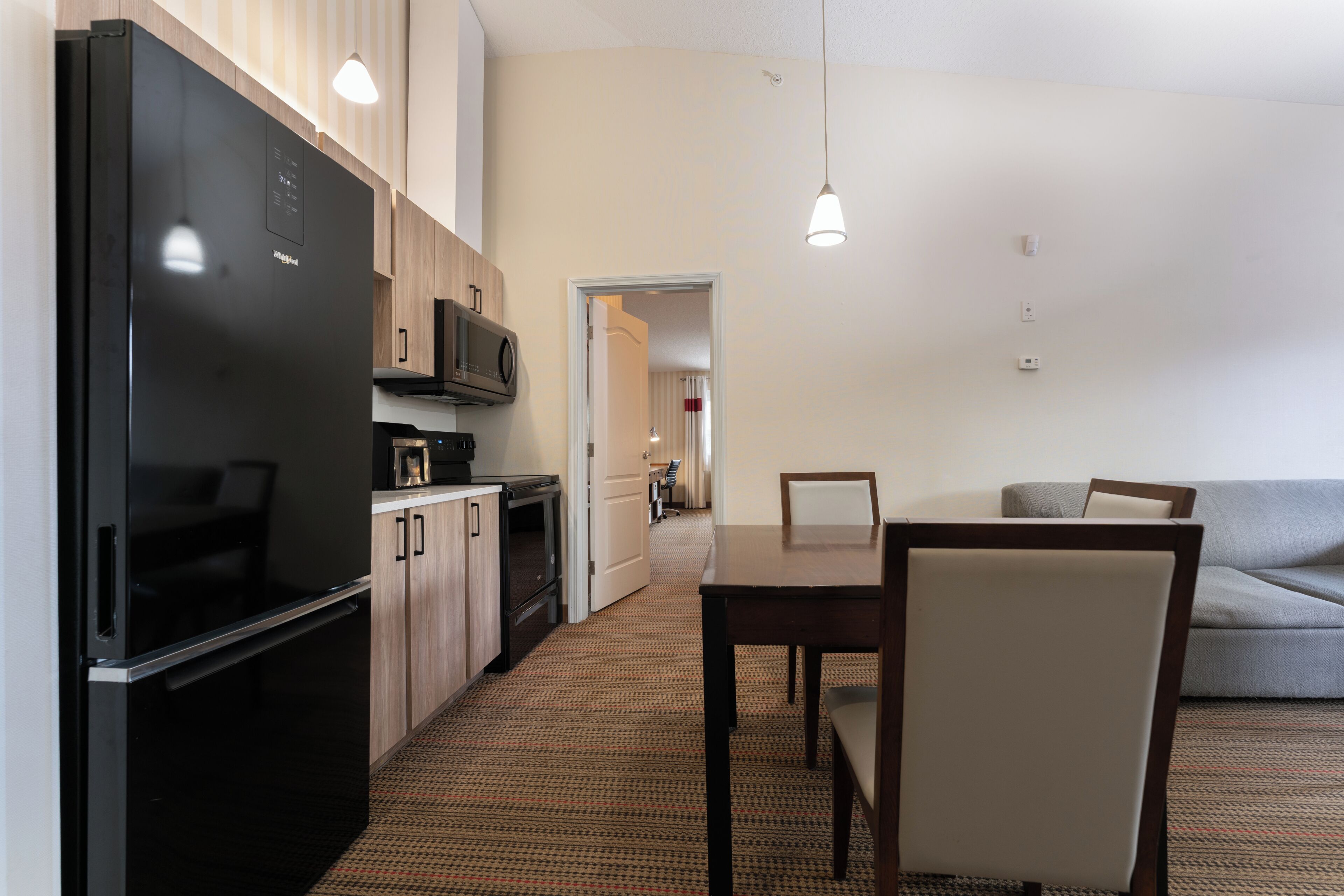 A compact kitchen with a refrigerator, microwave, and oven, leading to a dining area with a table and chairs.