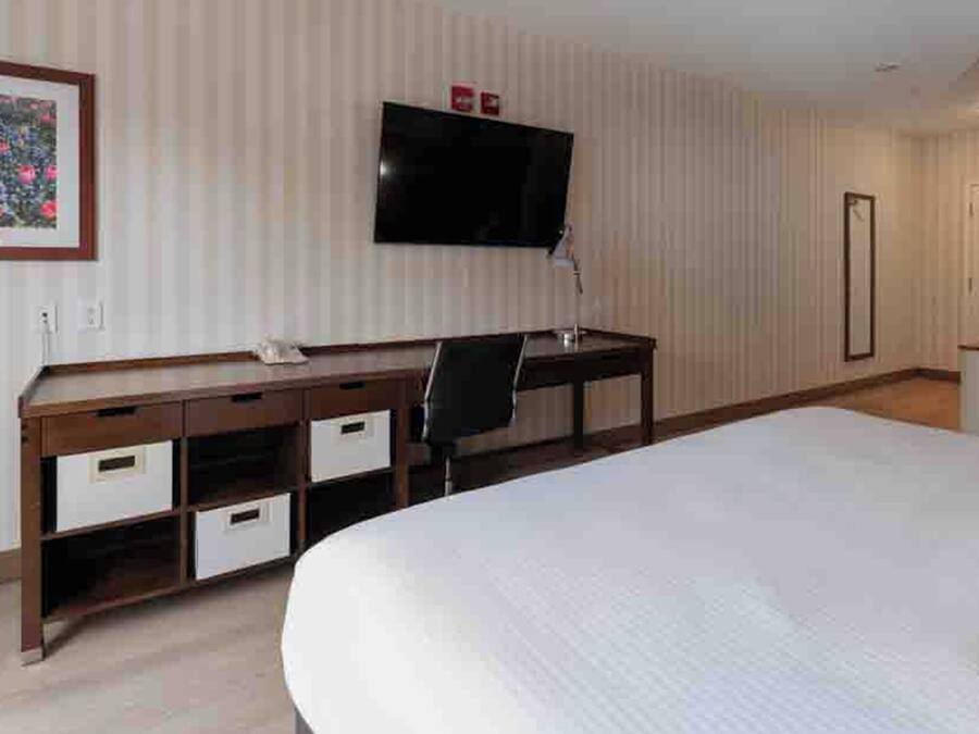 A hotel room with a bed, a desk with drawers, a chair, a television mounted on the wall, and a microwave on a counter.
