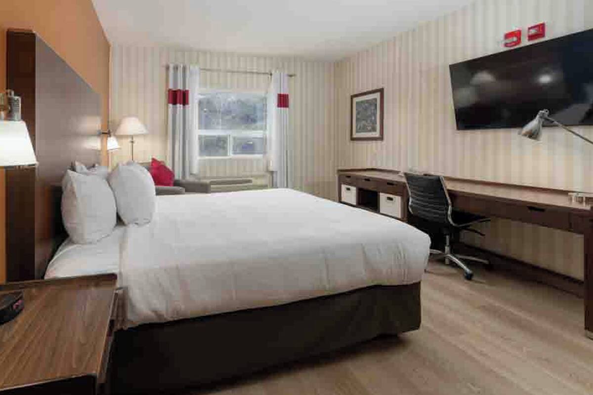 Ein Hotelzimmer mit Bett, Schreibtisch, Stuhl, Fernseher, Lampe und Fenster.