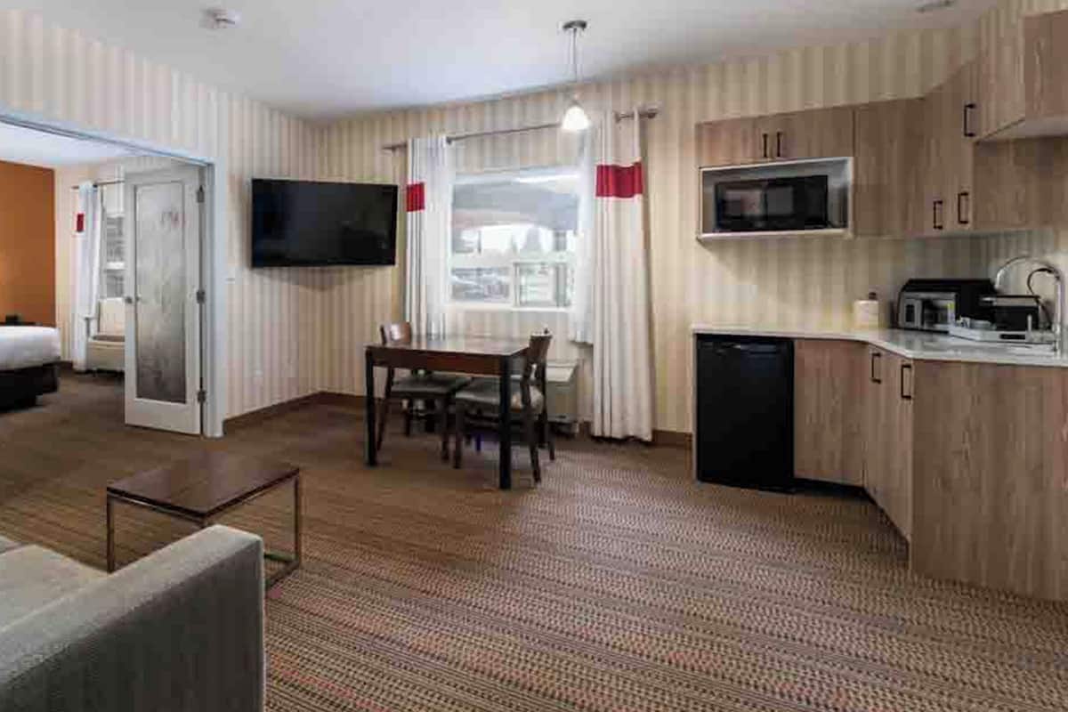 Ein Hotelzimmer mit Bett, Fernseher, Esstisch mit Stühlen, einer Küchenzeile und einer kleinen Sitzecke.