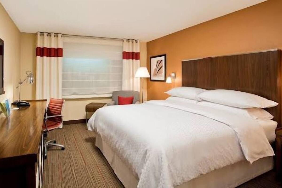 Ein Hotelzimmer mit Bett, Schreibtisch, Stuhl, Fernseher und einem Fenster mit Vorhängen.