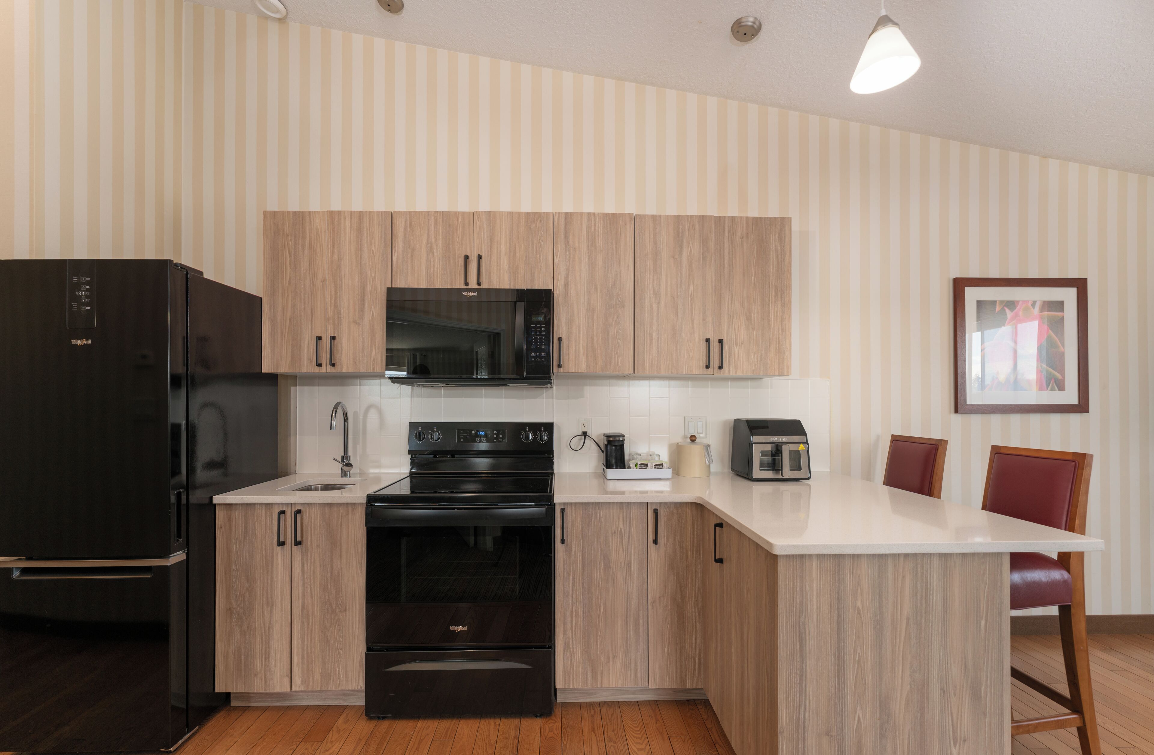 A modern kitchen with a refrigerator, microwave, oven, and a coffee maker on the countertop.