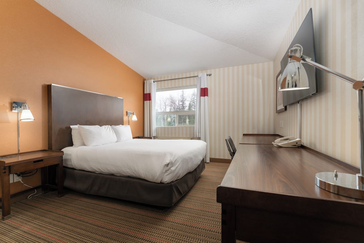Ein Hotelzimmer mit Bett, Nachttisch, Schreibtisch, Stuhl und einem an der Wand befestigten Fernseher.