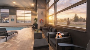 An indoor pool area with lounge chairs, a sofa, and a view of the sunset. - Prestige Prince George Lodge (Prince George)