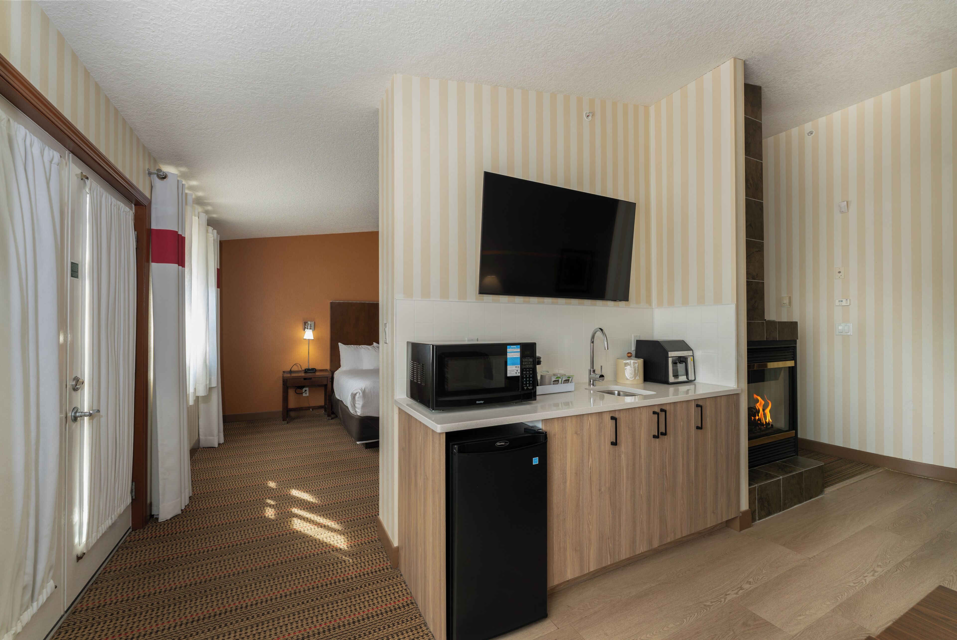 Une chambre d’hôtel compacte dotée d’une kitchenette, d’un téléviseur à écran plat, d’une cheminée et d’un lit.
