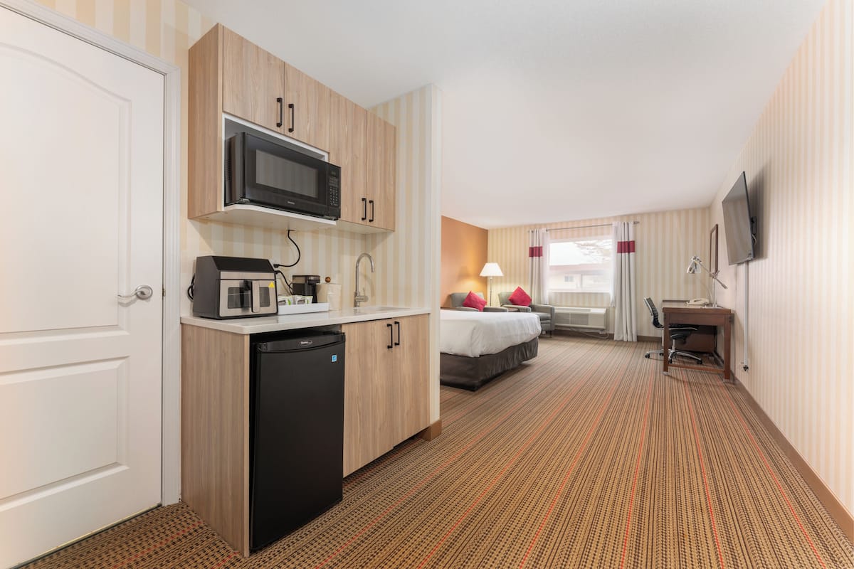 Ein Hotelzimmer mit Küchenzeile, einem Bett, einem Schreibtisch und einem Fernseher.