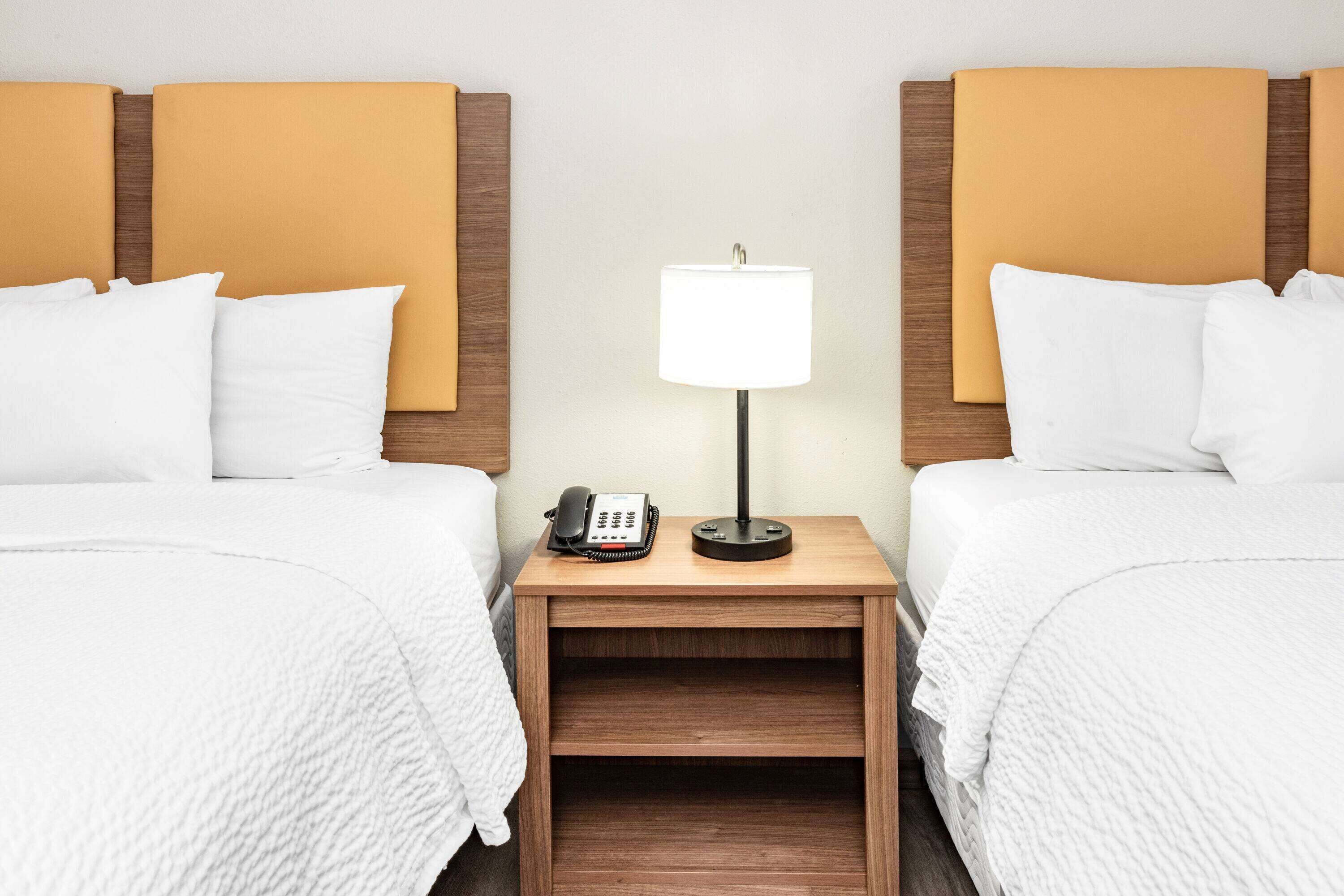 Quarto de hotel com duas camas, uma mesa de cabeceira com abajur e um telefone.