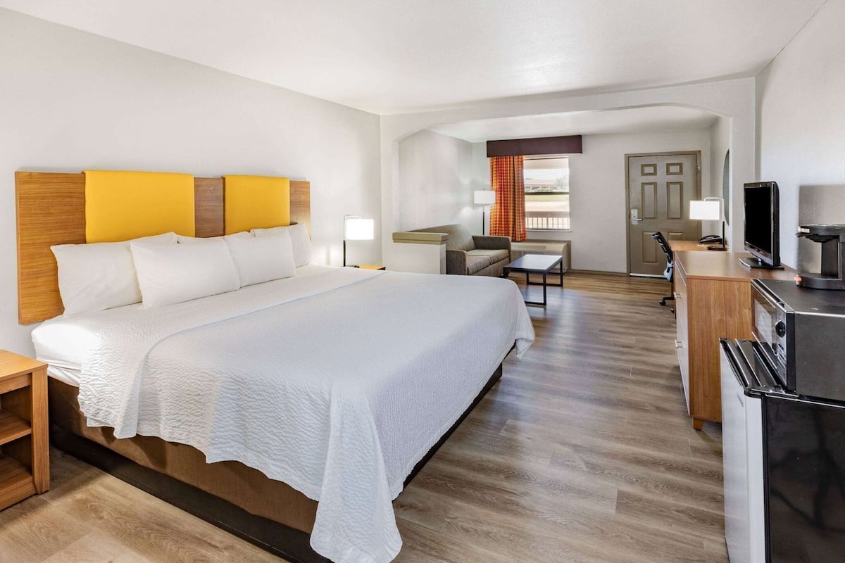 A hotel room with a large bed, a desk with a TV, a kitchenette, and a view of the outside.