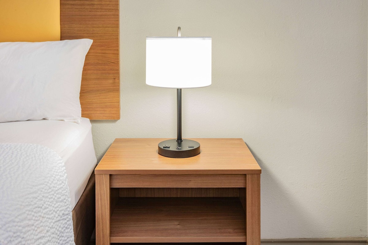A neatly made bed with a white pillow and a wooden nightstand with a lamp.