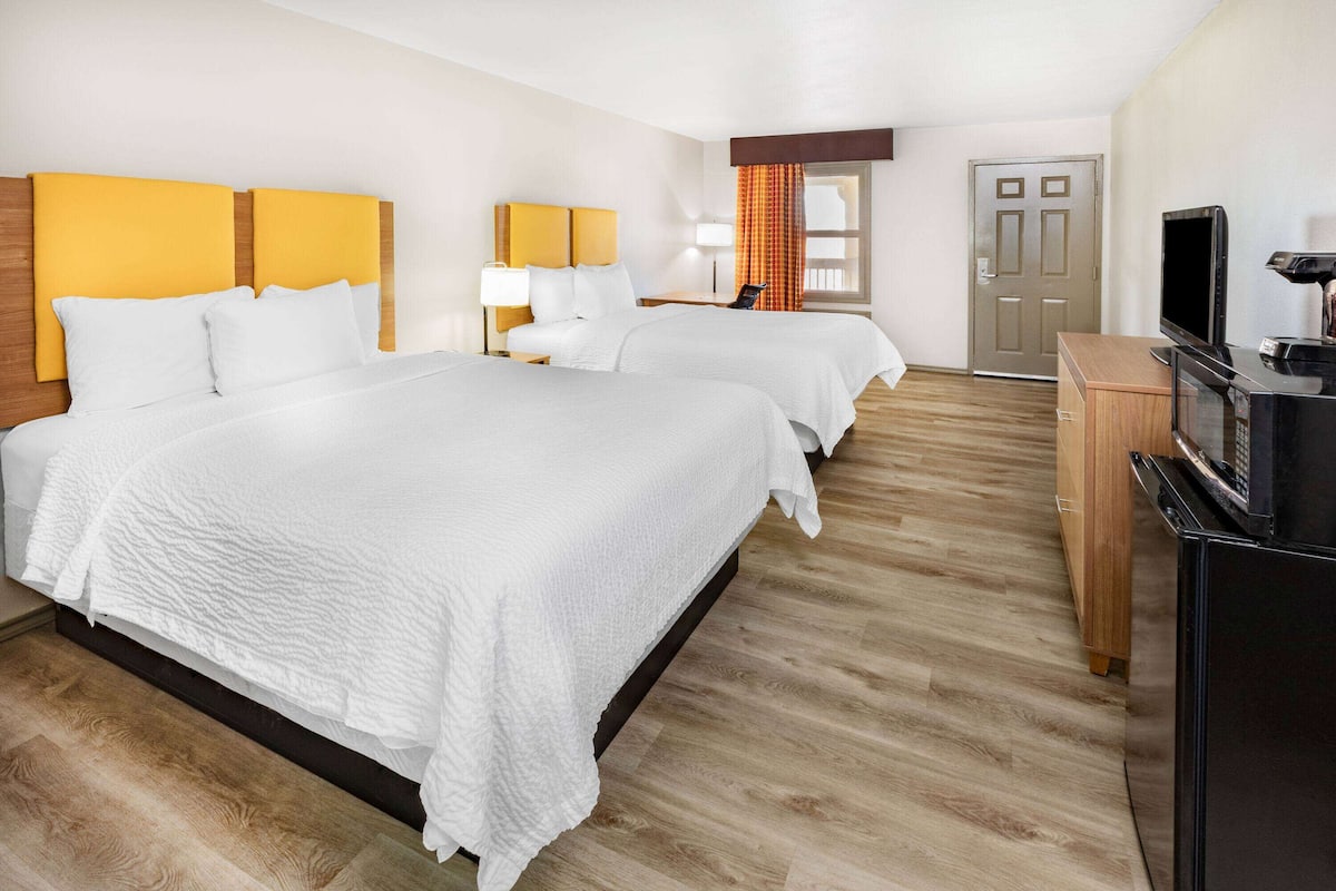 A hotel room with two beds, a TV, and a wooden cabinet.