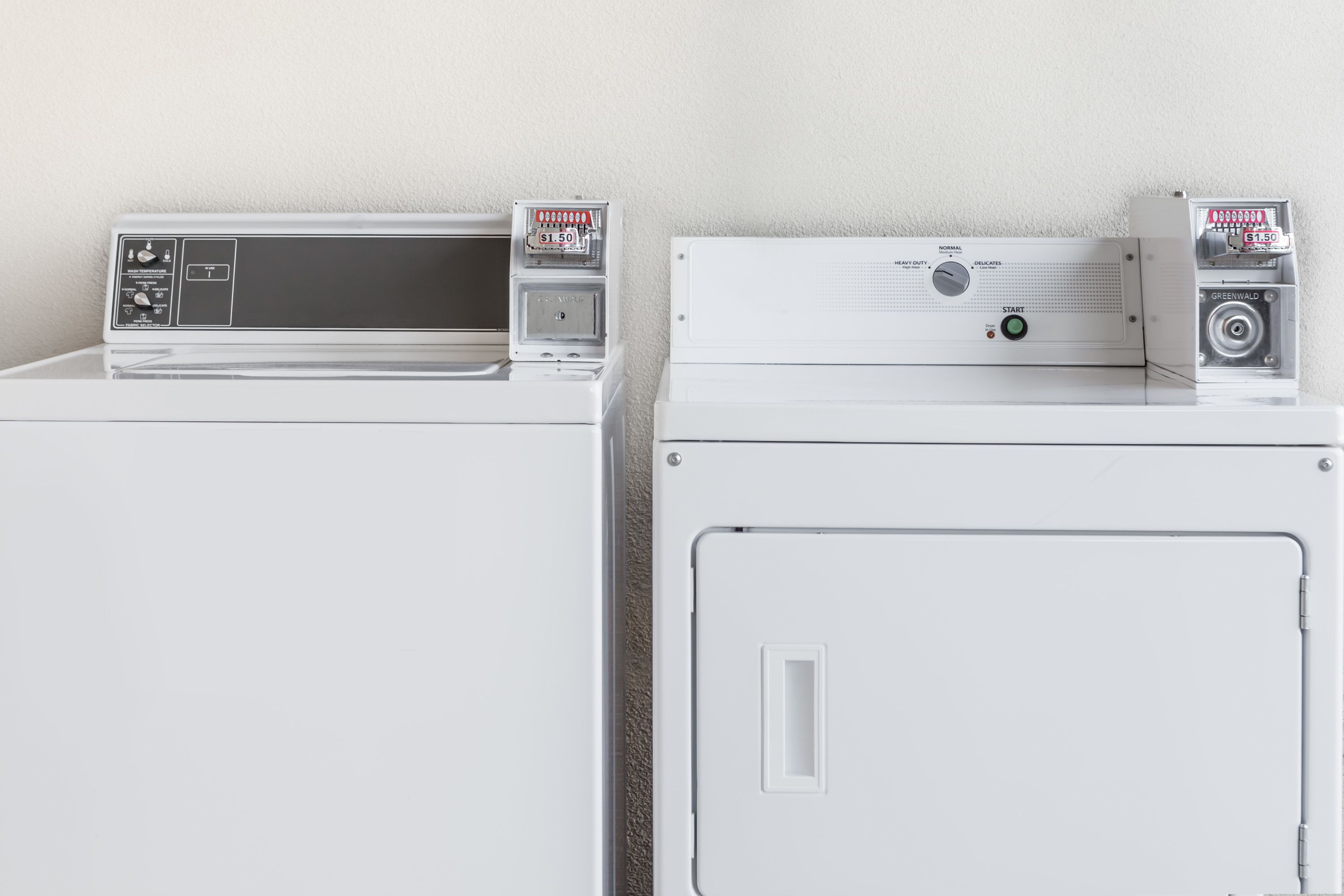 Two stacked washing machines with control panels and a coin slot.