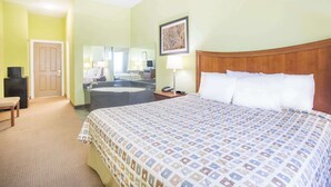A hotel room with a large bed, a desk, a chair, a bathroom with a bathtub, and a door. - Days Inn & Suites by Wyndham Swainsboro (Swainsboro)