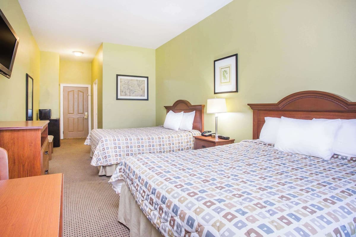 A hotel room with two beds, a desk, a chair, a TV, and a door.