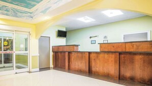 A reception area with a wooden reception desk, a 'Welcome!' sign, and a television mounted on the wall. - Days Inn & Suites by Wyndham Swainsboro (Swainsboro)