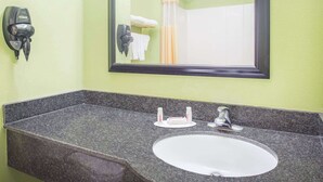 A bathroom with a granite countertop, a white sink, a mirror, a hairdryer, and a towel rack. - Days Inn & Suites by Wyndham Swainsboro (Swainsboro)