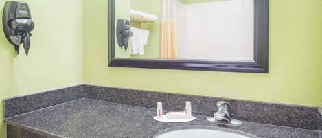 Un baño con encimera de granito, un lavabo blanco, un espejo, un secador de pelo y un perchero para toallas.