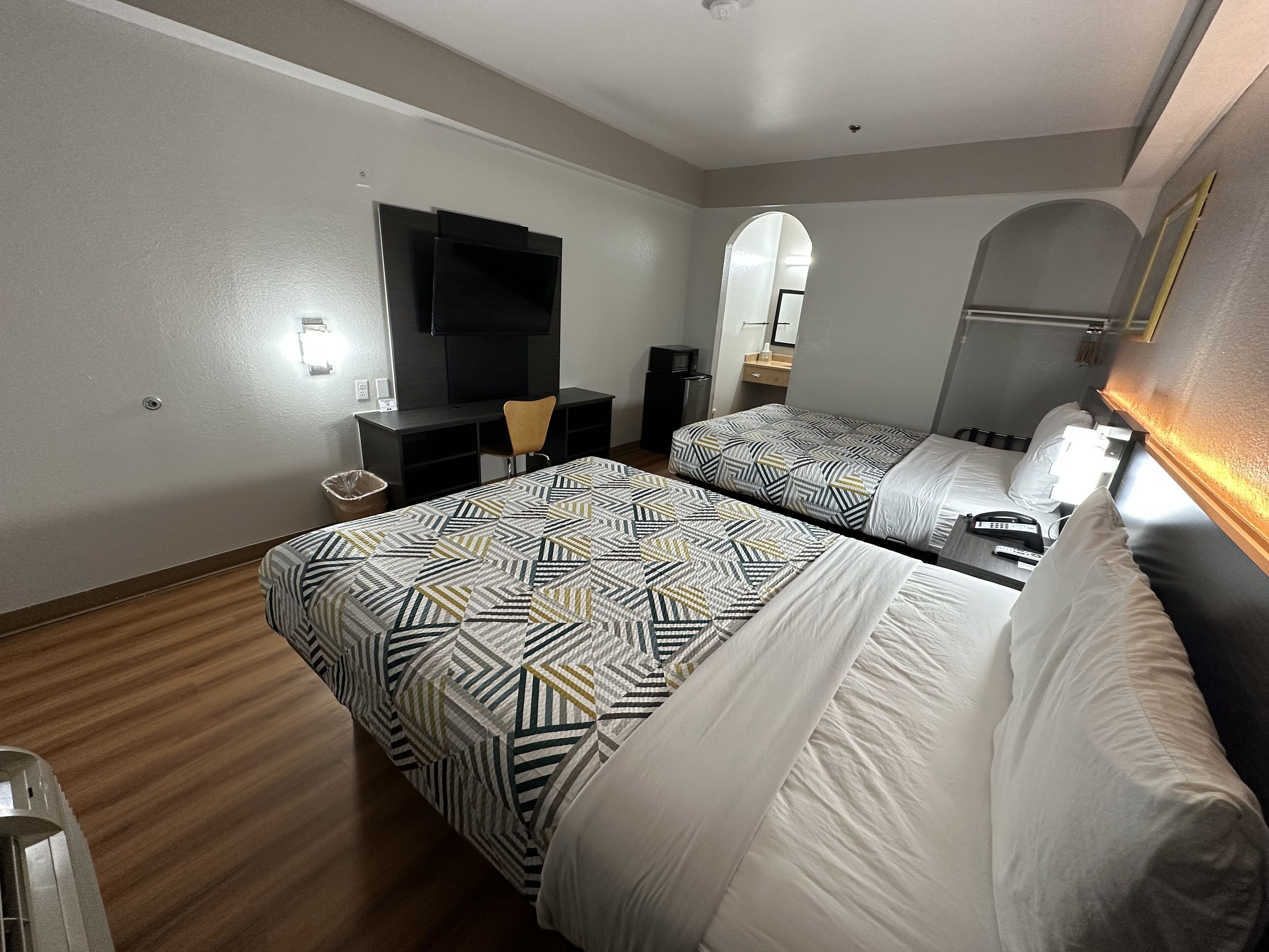 A hotel room with two beds, a desk, a chair, a TV, and a mirror.