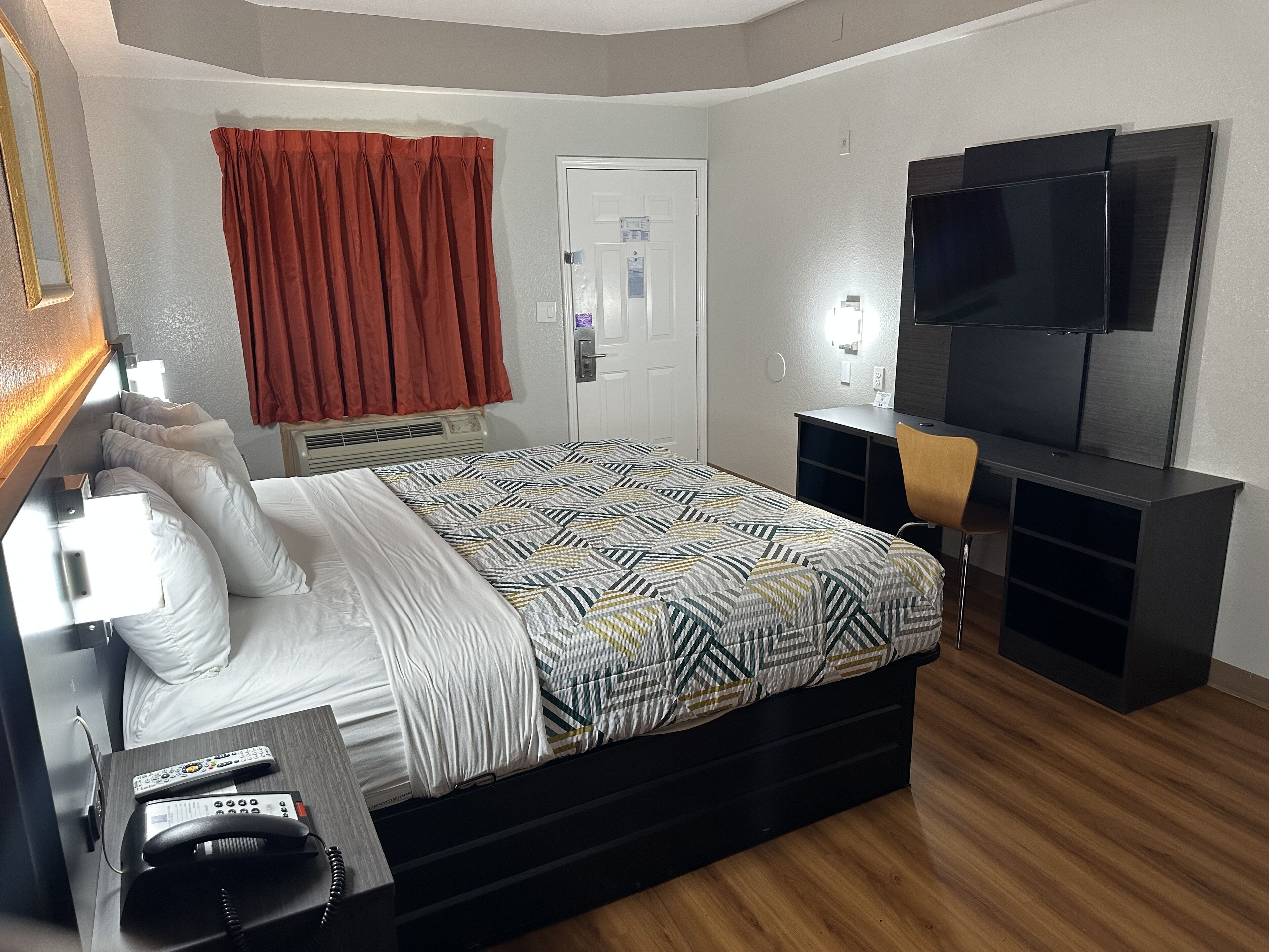A hotel room with a bed, a desk, a chair, a television, and a door.