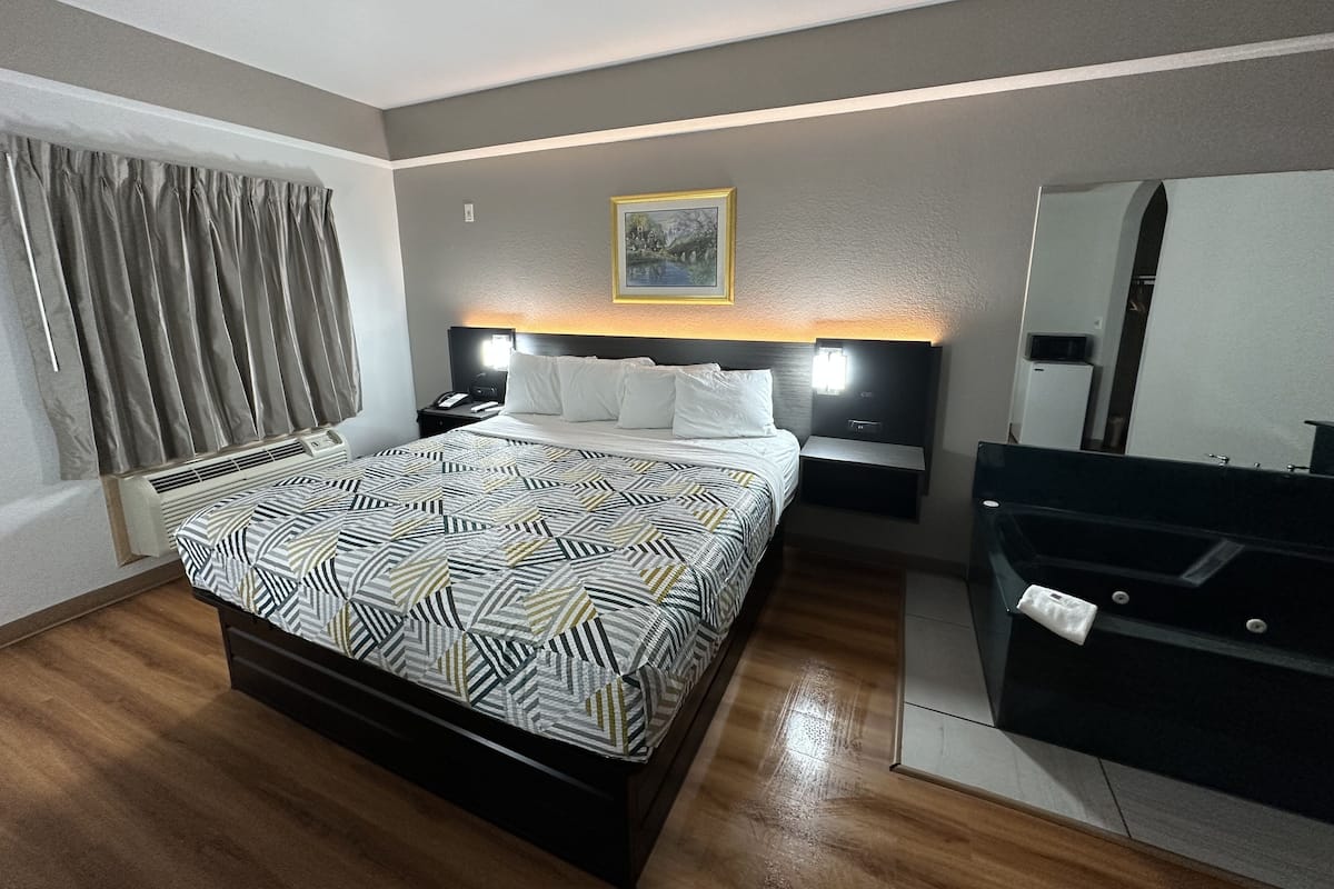 Une chambre d’hôtel moderne avec un grand lit, des tables de chevet, une commode, un bureau, un miroir et une fenêtre avec des rideaux.