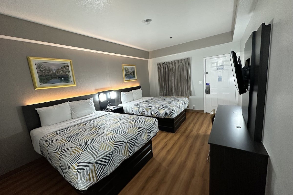 Une chambre d’hôtel avec deux lits, un bureau, une télévision et une porte.