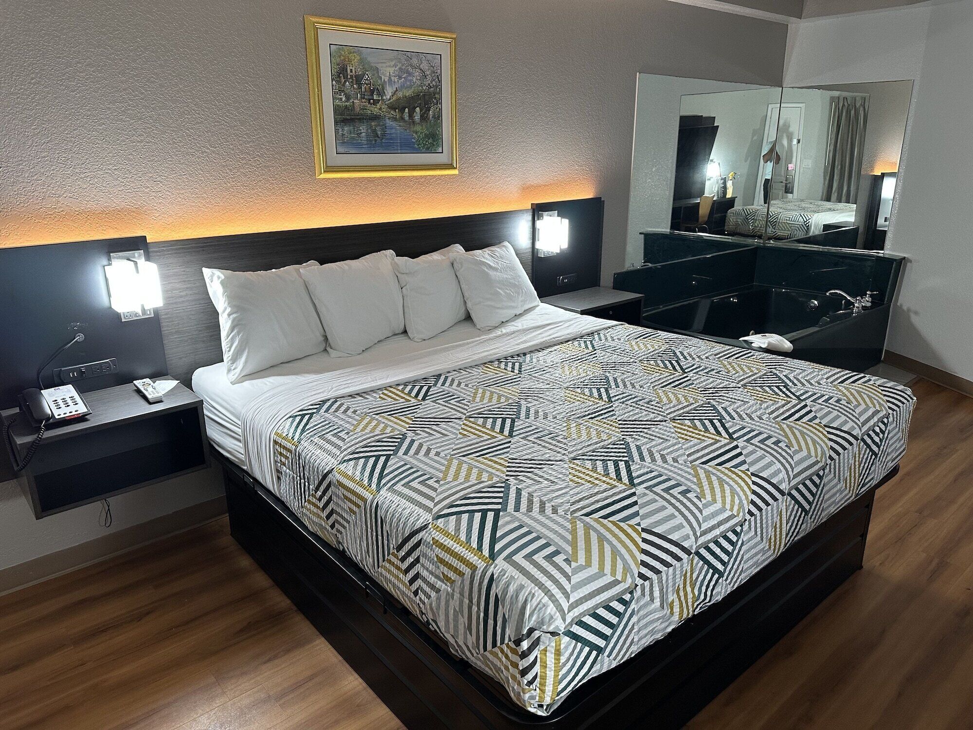 A modern hotel room with a large bed, a bedside table with a phone, a nightstand, a dresser, and a mirror.